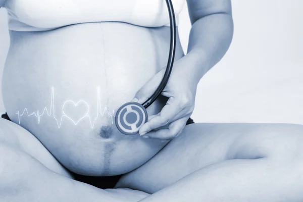 Pregnant woman with stethoscope and sign of heartbeats — Stock fotografie