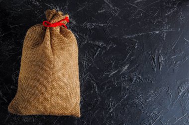 Kaba bir çuval bezinden yapılmış, koyu bir arka planda kırmızı sicimle bağlanmış, mesaj için yer açılmış bir Noel çantası. Boşluğu kopyala.