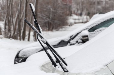 Snow-covered cars with raised wipers in a snow-covered Parking lot in an urban residential area clipart