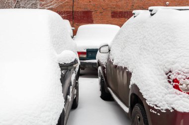 Şehrin yerleşim bölgesindeki karla kaplı bir otoparkta kalın bir kar tabakasıyla kaplı arabalar.
