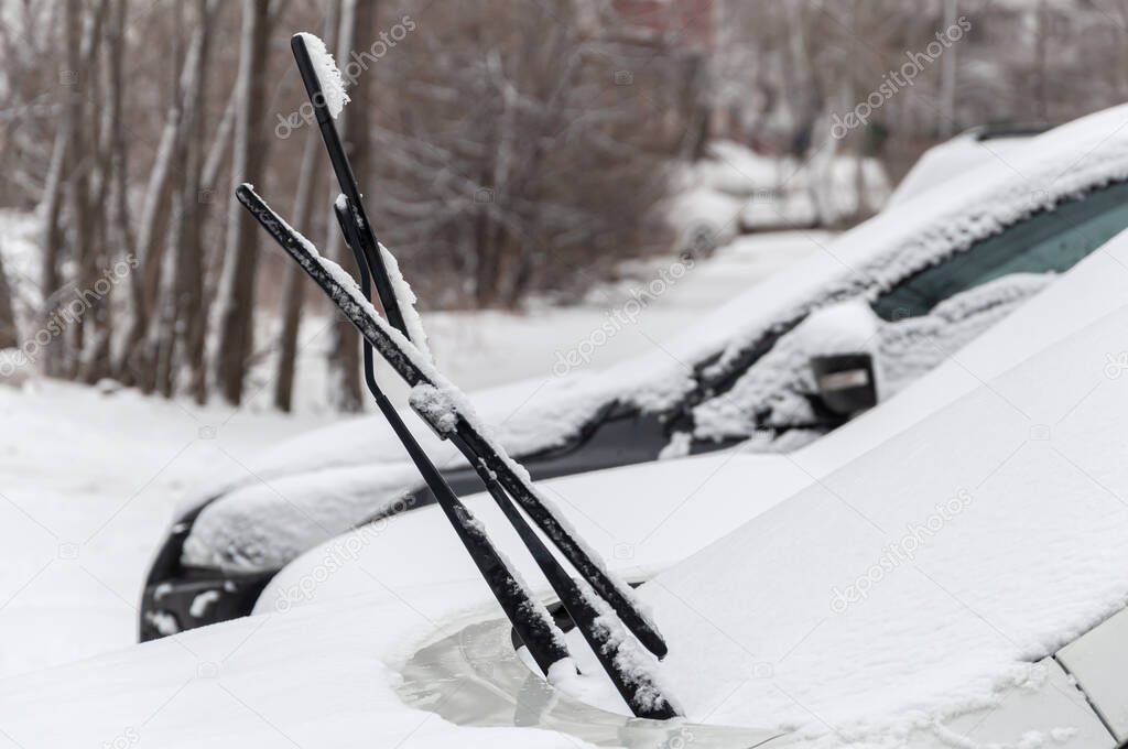 Snow-covered cars with raised wipers in a snow-covered Parking lot in an urban residential area