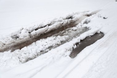 Asfalt yüzeyinde erimiş kar, derin durgun su ve kenarlarında kar. Baharın başında karlı bir yolda su birikintileri.