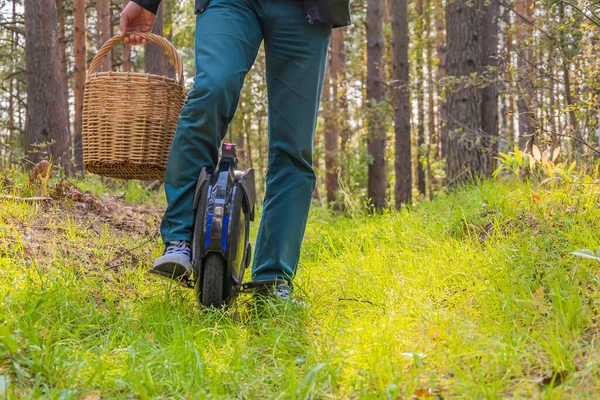 Front view of men\'s legs on an electric unicycle in the forest. A man with a wicker basket on an electric monowheel.