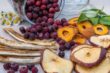Dilimlenmiş kurutulmuş elma, kayısı ve muz, cam bir kavanozda kurumuş kiraz, ışık masasında nane yaprakları. Kurutucuda kurutulmuş meyve pişirme konsepti.