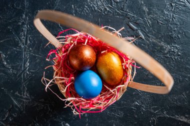 Ev yapımı çok renkli Paskalya yumurtaları siyah arka planda hasır bir sepette renkli saman üzerinde.