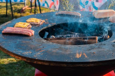 Açık havada büyük yuvarlak ahşap ızgarada, sosisler, sosisli çörekler, hamburgerler için peynirli sığır köfteleri kızartılır. Şehir parkında barbekü festivali.