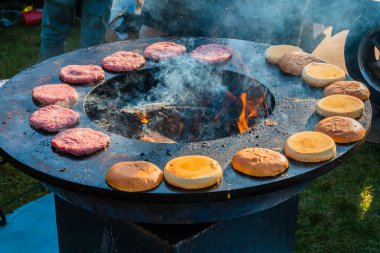 Biftek köfteleri ve hamburger çörekleri dışarıdaki büyük, yuvarlak ahşap ızgarada kızartılıyor. Şehir parkında barbekü festivali. Sokak Fast food.