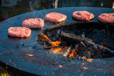 Hamburgerler için sığır köfteleri büyük yuvarlak ahşap ızgarada kızartılıyor. Yakın plan. Şehir parkında barbekü festivali. Sokak Fast food.