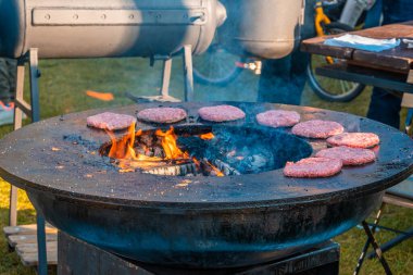 Çimenlikte, büyük yuvarlak ahşap ızgara hamburger için köfte kızartıyorlar. Şehir parkında barbekü festivali. Sokak Fast food.