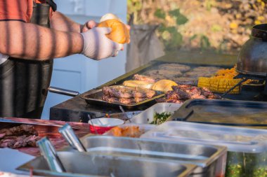 Hamburger pişiriyorum. Profesyonel bir şef hamburger hazırlar. Şehir parkında barbekü festivali. Sokak Fast food.