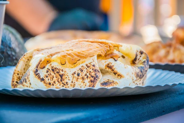 Mexican food, a steak burger wrapped in a tortilla under melted cheese on the counter of an outdoor restaurant. Food festival in the city park. Street fast food. Selective focus.