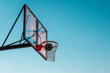 Mavi arka planda topu olan bir basketbol sepeti. Açık hava basketbol sahasında şeffaf plastik basketbol kalkanı..