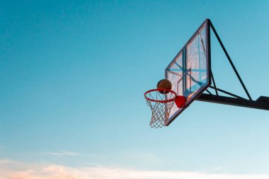 Mavi arka planda topu olan bir basketbol sepeti. Açık hava basketbol sahasında şeffaf plastik basketbol kalkanı..