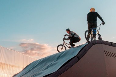 Şehir parkındaki kaykay parkının rampasında bisiklete binen genç sürücüler dinlenmek için.