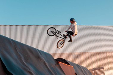 Bir BMX sürücüsü açık hava aktiviteleri için şehir parkındaki bir kaykay parkında bir rampada gösteri yapıyor.
