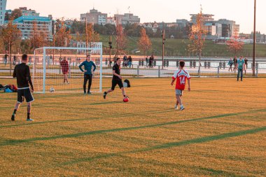 Genç futbolcular bir yaz akşamı şehir parkında sahada futbol oynarlar..