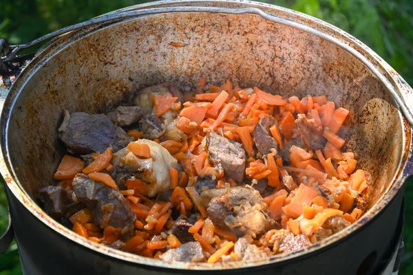 Sliced carrots and pieces of meat in a cauldron in the process of cooking pilaf on a traditional Asian oven. Step-by-step recipe for real pilaf.