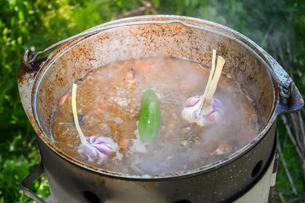 Hot pepper and garlic heads in boiling water, covering sliced carrots and pieces of meat in a cauldron in the process of cooking pilaf on a traditional Asian oven. Step-by-step recipe for real pilaf