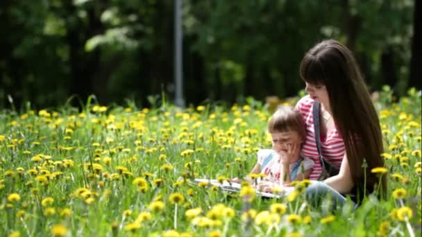 Joven madre y su hija leen un libro para niños al aire libre — Vídeo de stock