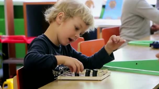 Boys play checkers in kindergarten. They are passionate about the game, laugh, rejoice. — Stock Video