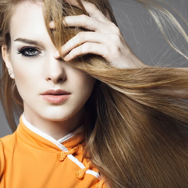 Porträtt av en vacker ung blond flicka i studion på en grå bakgrund med att utveckla hår, begreppet skönhet — Stockfoto