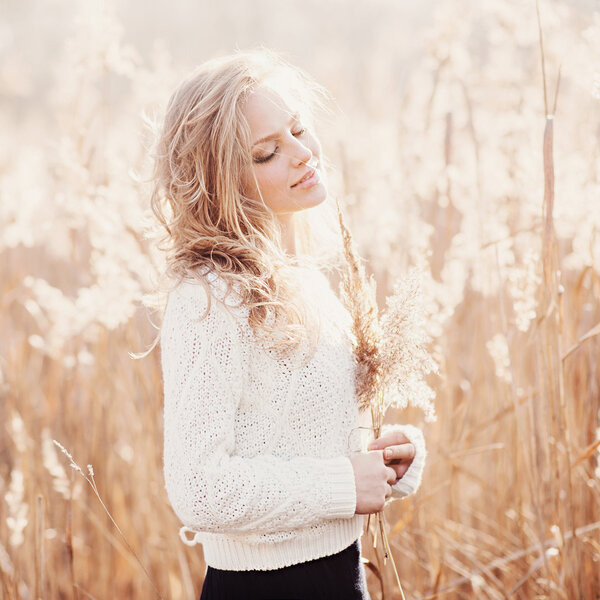 Portrait of a beautiful blonde girl in a field in white pullover, smiling with eyes closed, concept beauty and health