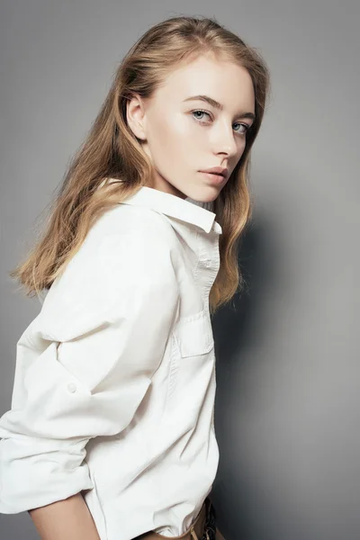 Portréja egy gyönyörű, fiatal szőke nő egy fehér inget, a stúdióban egy szürke háttér — Stock Fotó