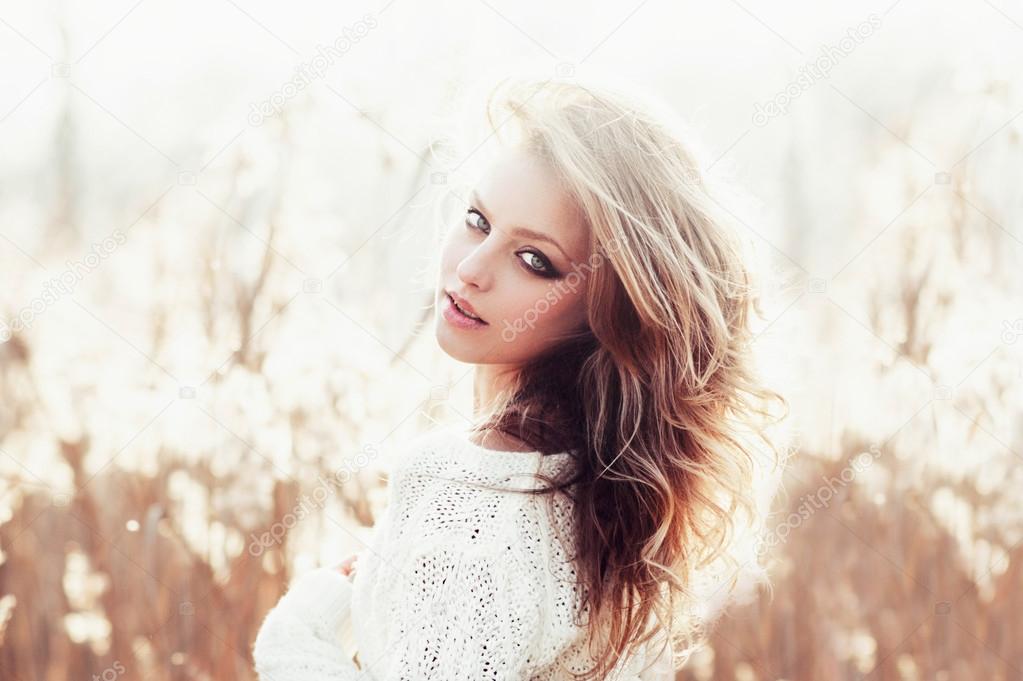 Sunny portrait of a beautiful young blonde girl in a field in white pullover, the concept of health and beauty