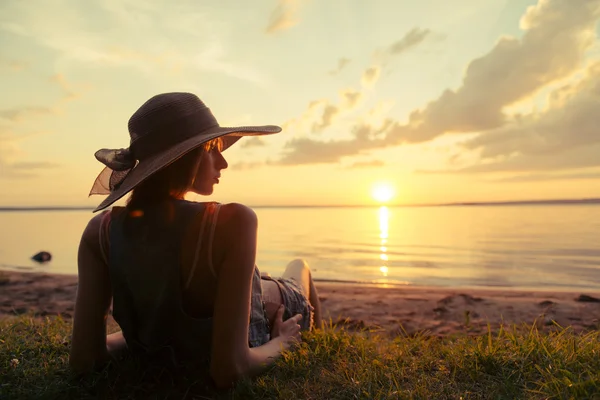 Žena sedí na pláži při západu slunce — Stock fotografie