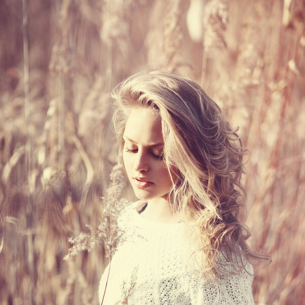 Portrait of pensive beautiful blonde girl in a field in white pullover, the concept of health and beauty