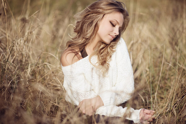 Portrait of beautiful young girl in an autumn field in white pullover, life style