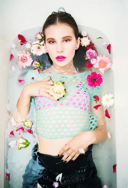Retrato de bela jovem morena com maquiagem brilhante deitada no banho com flores, o conceito de saúde e beleza — Fotografia de Stock