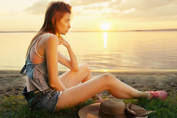 Žena sedí na pláži při západu slunce — Stock fotografie