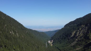 Tepeleri, ormanı ve köyü olan bir panorama.