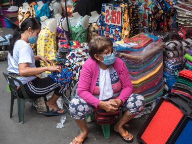 Divisoria, Manila, Filipinler - Ekim 2020: Orta yaşlı bir kadın satıcı ve yardımcısı sokak pazarında kıyafet satıyor.