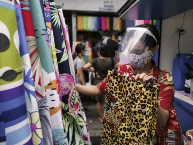 Divisoria, Manila, Filipinler - Ekim 2020: Sokak pazarındaki yerel bir tezgahta çarşaflar için yüz maskesi ve kalkan dükkanları takan bir kadın.