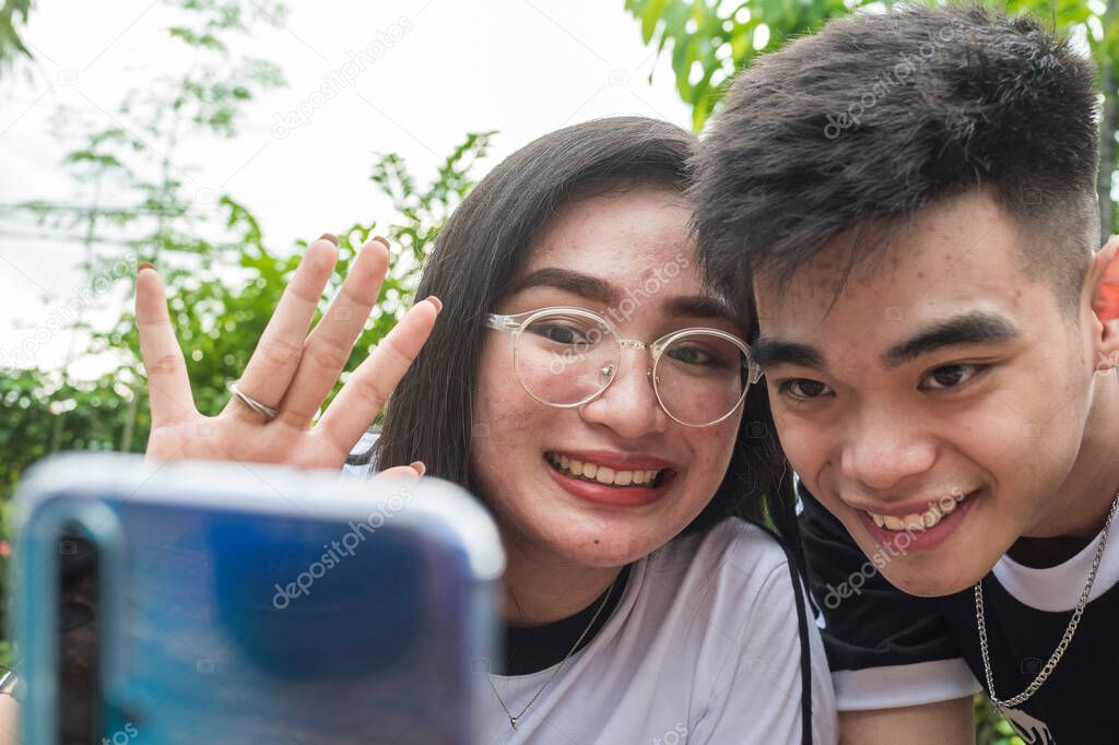 A young southeast asian couple talk to their friend via videocall on a smartphone placed on a phone holder. Modern Generation Z lifestyle concept.