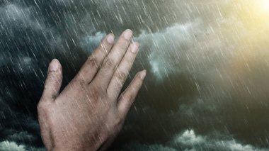 Dua eden ellerin birleşimi ve sağında parlak bir ışık olan yağmur ve fırtına bulutları. Doğal afetler arasında dua ve umut kavramı - sağanak yağmurlar, fırtınalar, tayfunlar ve diğer kötü hava koşulları.