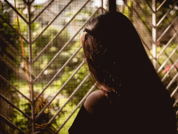 Silhouette of a young woman grieving indoors. A an indoor patio with large iron grilles. Distress, loss, or sadness concept.