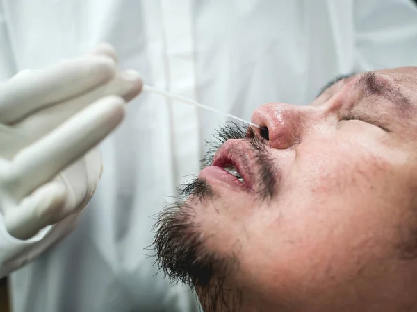アジア人男性は 彼の鼻に部分的に挿入された軍不快な鼻咽頭スワブ迅速なテストを受けます 本物のCovid鼻波検査と患者からの反応 白衣を着た匿名の看護師 — ストック写真