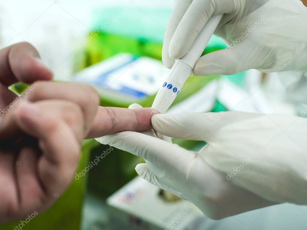 Closeup view of a finger prick blood test. A patient is tested for Covid-19 via rapid antibody test using a disposable blood lancet. Possible test for blood sugar level too.