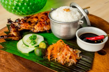 Chicken Inasal served with Garlic Rice, cucumber and Atchara. On a banana leaf on top of wooden platter. It is popular grilled dish from the Western Visayas region of the Philippines clipart