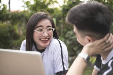 Genç bir Filipinli kız dışarıda dizüstü bilgisayarda yaptığı bir inceleme sırasında erkek arkadaşıyla konuşurken gülümsüyor..