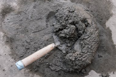 Küçük bir beton yığını ve içinde kısmen gömülü bir mala. Yere yerleştirilmiş. Daha büyük bir yığın karışık beton kalıntısı..