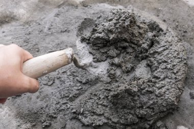 Bir el, beton dolu bir malayı küçük bir çimento yığınından yakalar. Dışarıdaki beton zeminde..