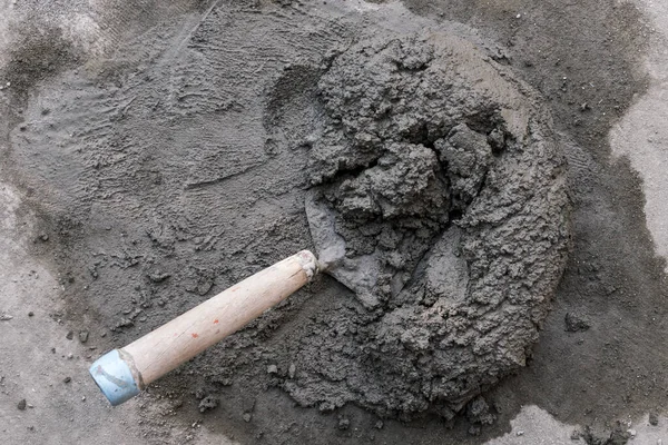 Küçük bir beton yığını ve içinde kısmen gömülü bir mala. Yere yerleştirilmiş. Daha büyük bir yığın karışık beton kalıntısı..