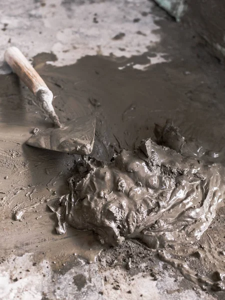 Yanında kürek olan bir yığın ıslak çimento. Beton zemine dikkatsizce yerleştirilmiş. Fayanslar, tamirat ya da DIY için küçük bir proje.