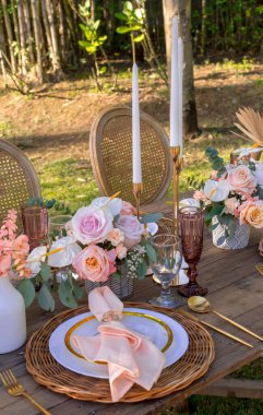 Açık hava bahçe düğününde güzel bir kır sofrası. Beyaz uzun mumlar ve pastel masa üstü süsü. Açık hava ziyafeti, dışarıda.