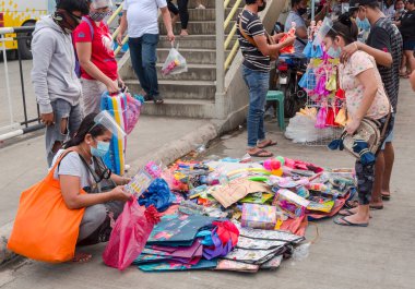 Taytay, Rizal, Filipinler - Aralık 2020: Bir satıcı kaldırımda ve üst geçidin yakınında ucuz oyuncaklar satıyor. İlgilenen birkaç müşteri en iyilerini kontrol ediyor. Yüz maskeleri ve kalkanları var..