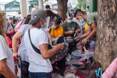 Divisoria, Manila, Filipinler- Bir sokak satıcısı tarafından satılan ucuz tişörtleri almak için sıraya girmiş bir müşteri topluluğu. Hepsi maske takıyor ama sosyal mesafeyi zar zor gözlemliyorlar..